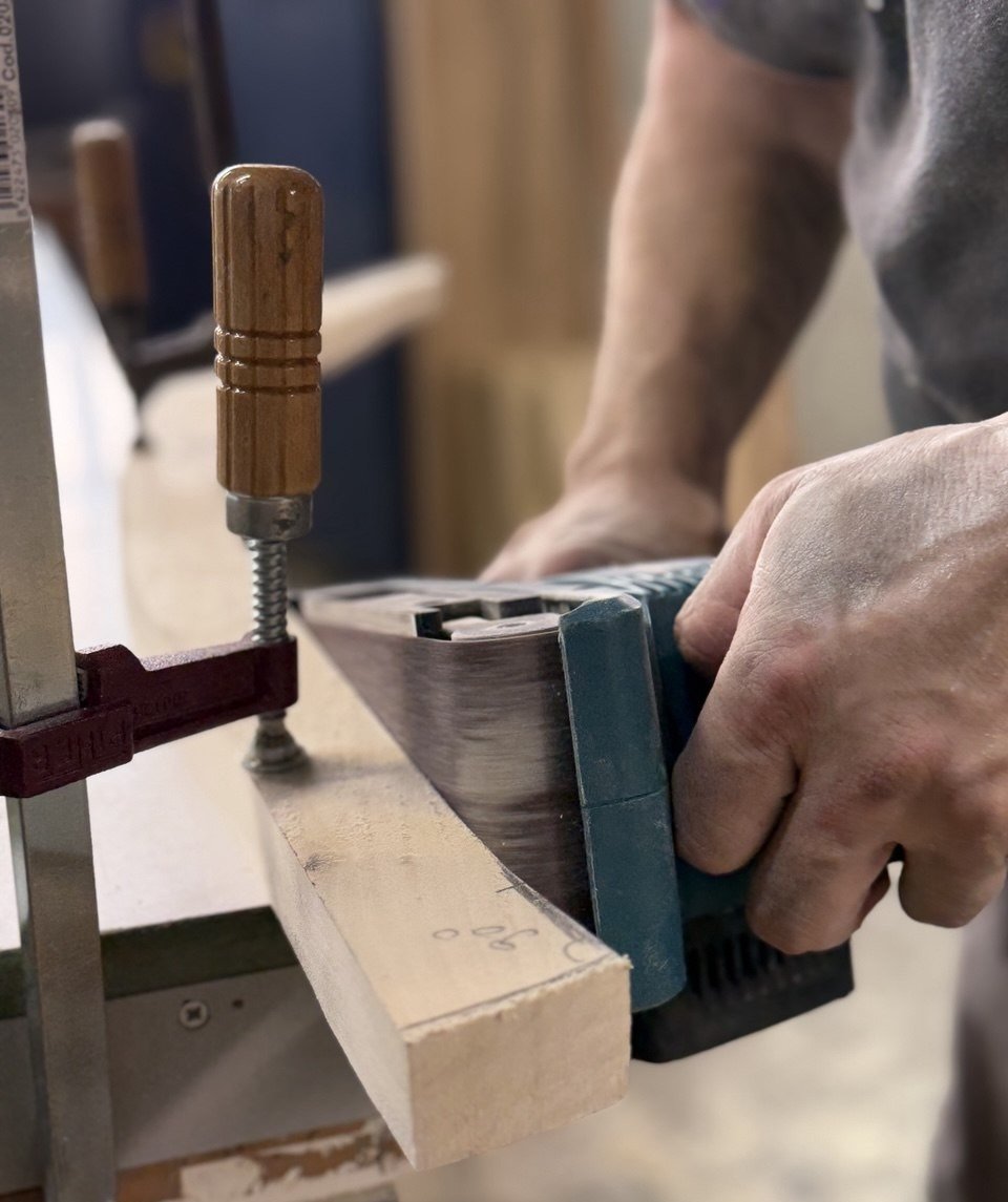 A craftsman sanding a clamped piece of solid wood at the workbench