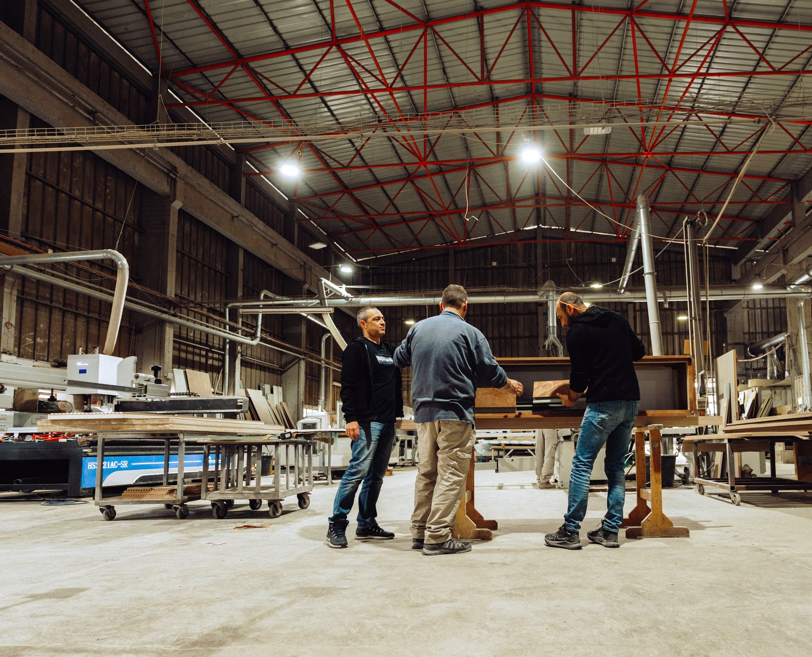 Three ArtiArt craftsmen reviewing a timber panel together at the workbench in the workshop
