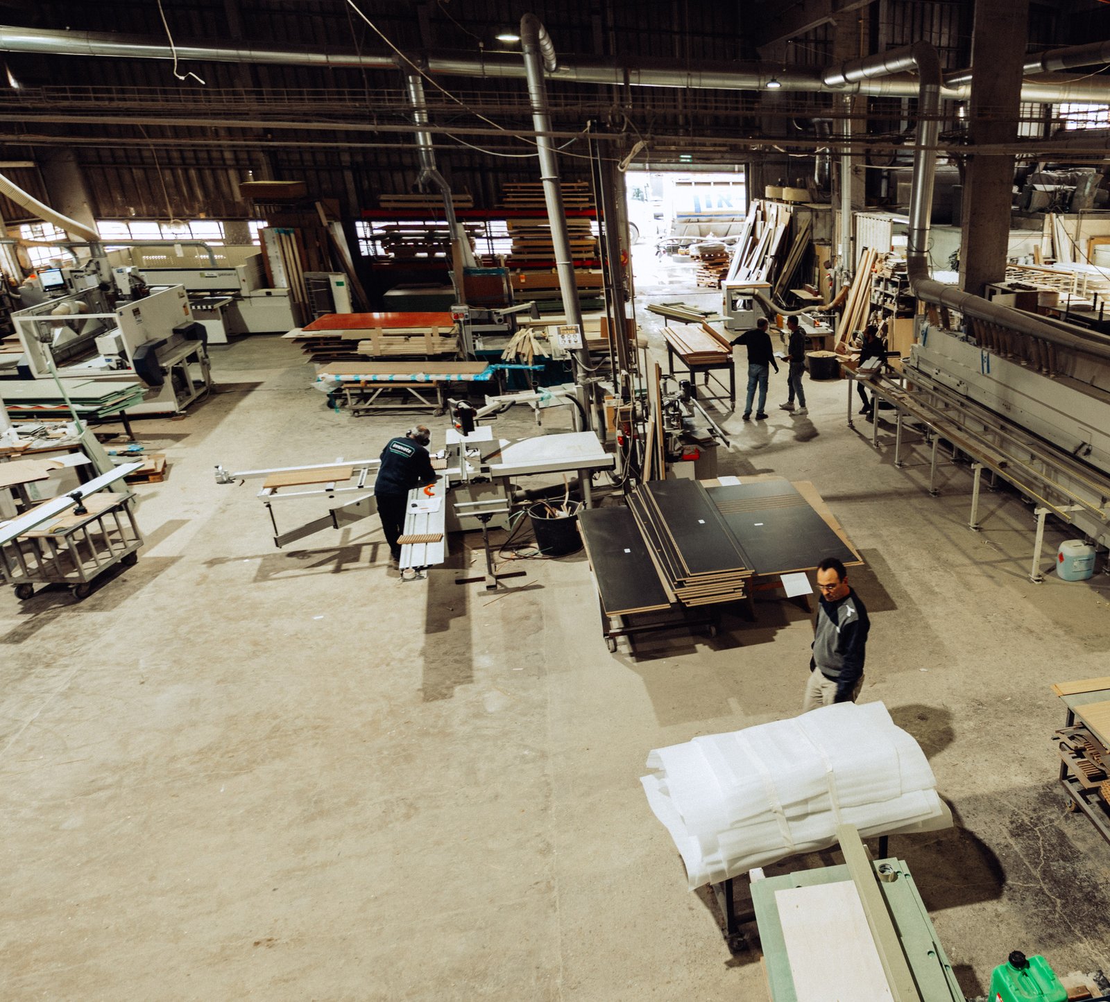 Overview of the ArtiArt workshop with craftsmen cutting, edge-banding and assembling timber panels