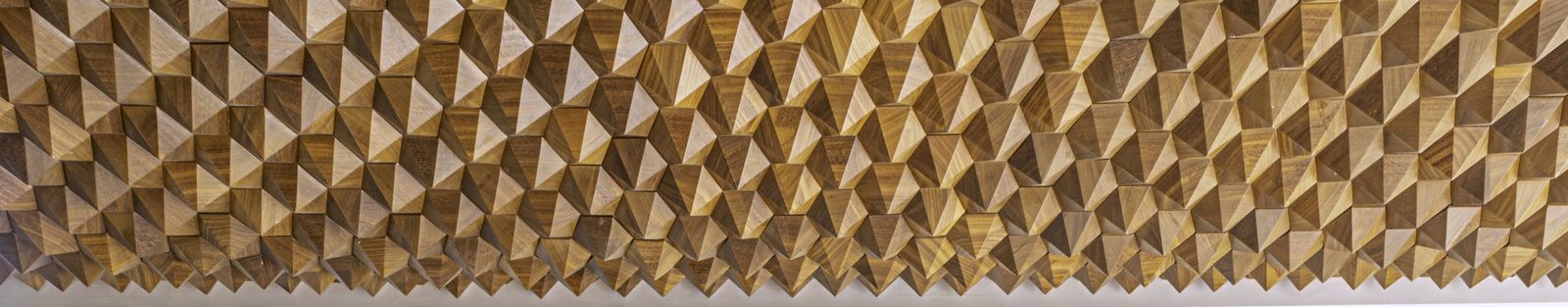 A full-width wall of hand-faceted walnut blocks catching raking light