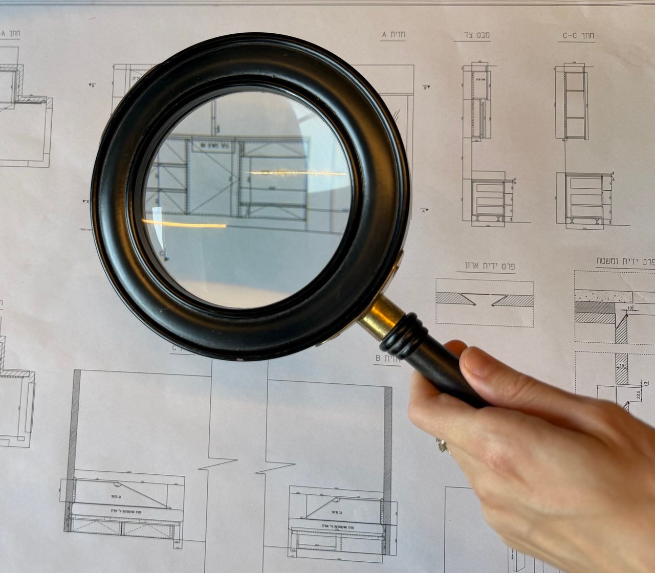 A magnifying glass held over detailed furniture shop drawings